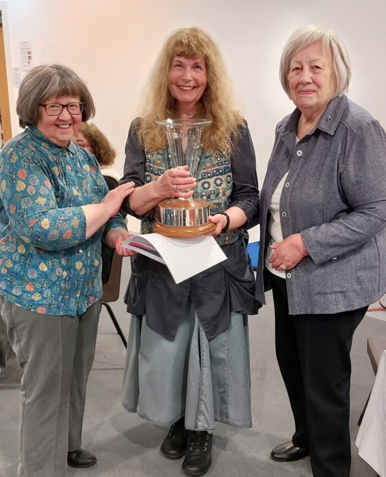 Maggie Powell, winner of the Margaret Thomson Davis Trophy presented this year for a children's story, with adjudicator, betty Mckay and Competion secretart, Adrienne Whitehall. Maggie holds the trophy, a tall fluted glass vase on a circular wooden base.